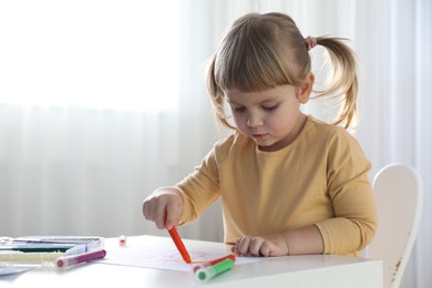 Cute little girl drawing with marker at white table indoors. Child`s art