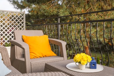Photo of Orange pillow and yellow chrysanthemum flowers on rattan garden furniture outdoors