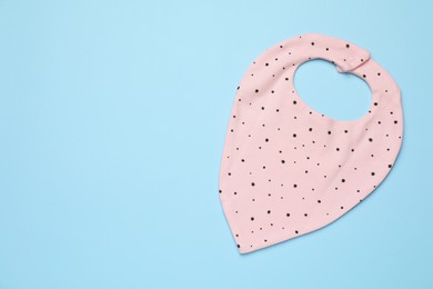 New baby bib on light blue background, top view. Space for text