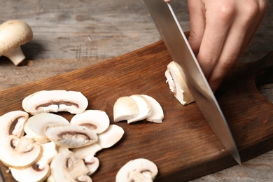 Photo of Young woman cutting fresh champignon mushrooms on wooden board, closeup view