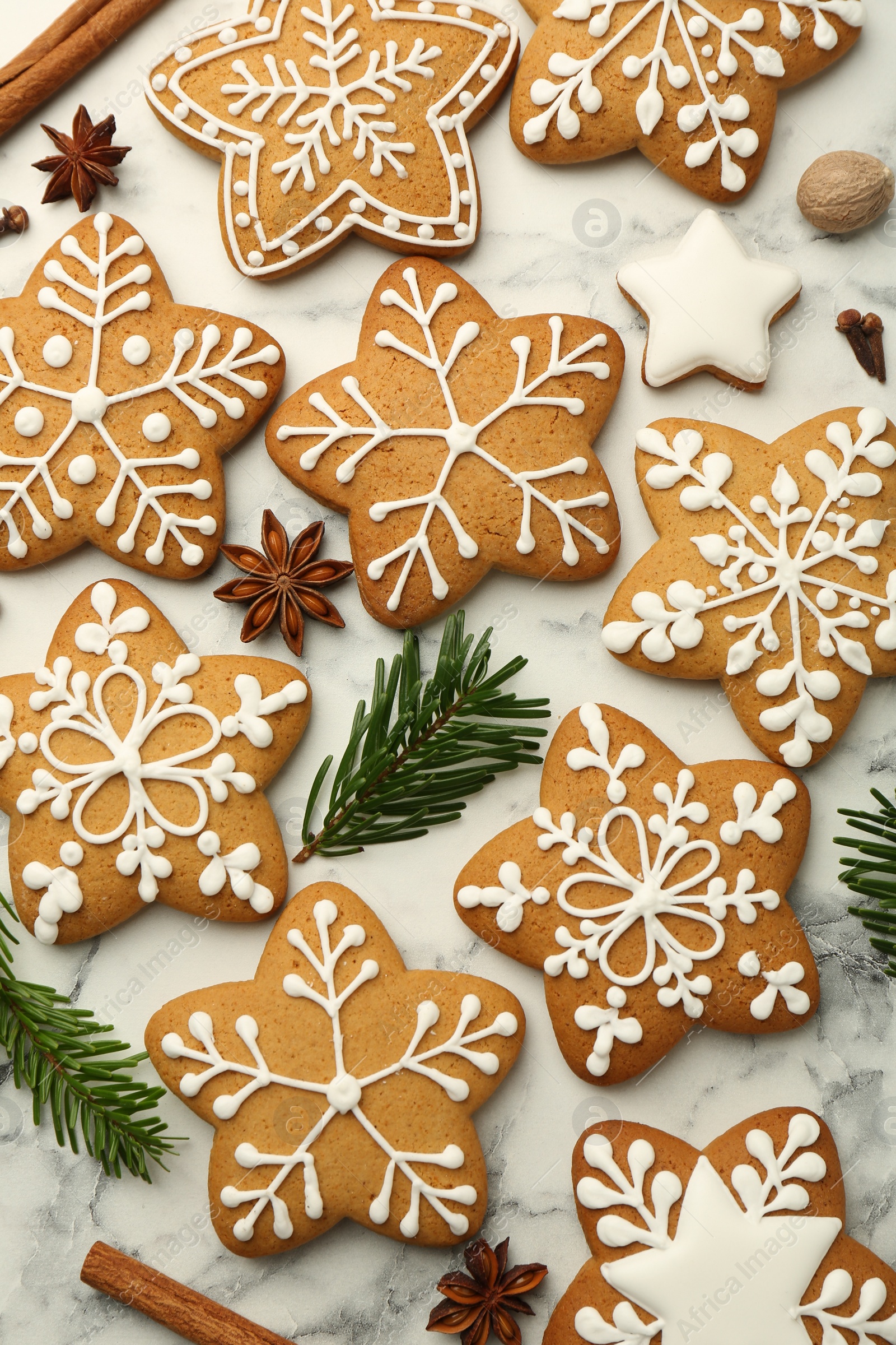 Photo of Tasty star shaped Christmas cookies with icing, spices and fir tree twigs on white marble table, flat lay