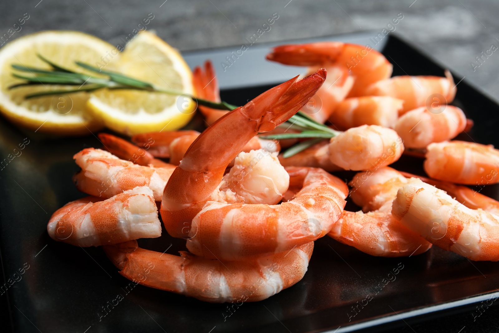 Photo of Delicious cooked shrimps with rosemary and lemon on black plate, closeup