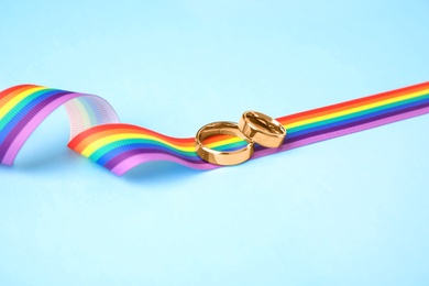 Wedding rings and rainbow ribbon on color background. Gay symbol