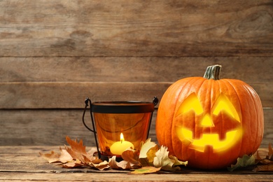 Scary jack o'lantern pumpkin and burning candle on wooden table, space for text. Halloween decor