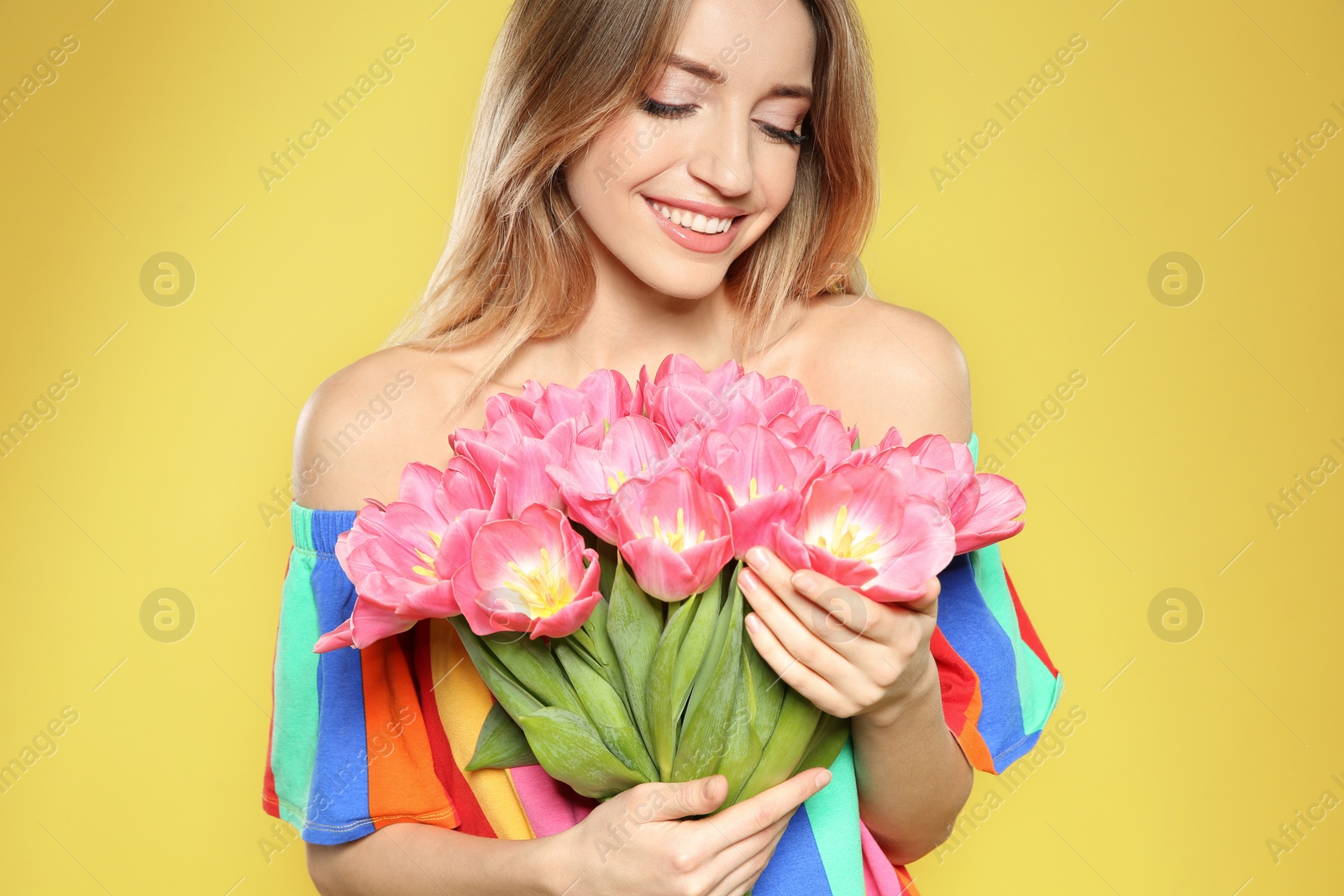 Photo of Portrait of beautiful smiling girl with spring tulips on yellow background. International Women's Day