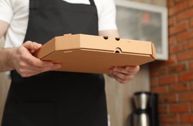 Photo of Waiter in apron with pizza box indoors, closeup. Food delivery service