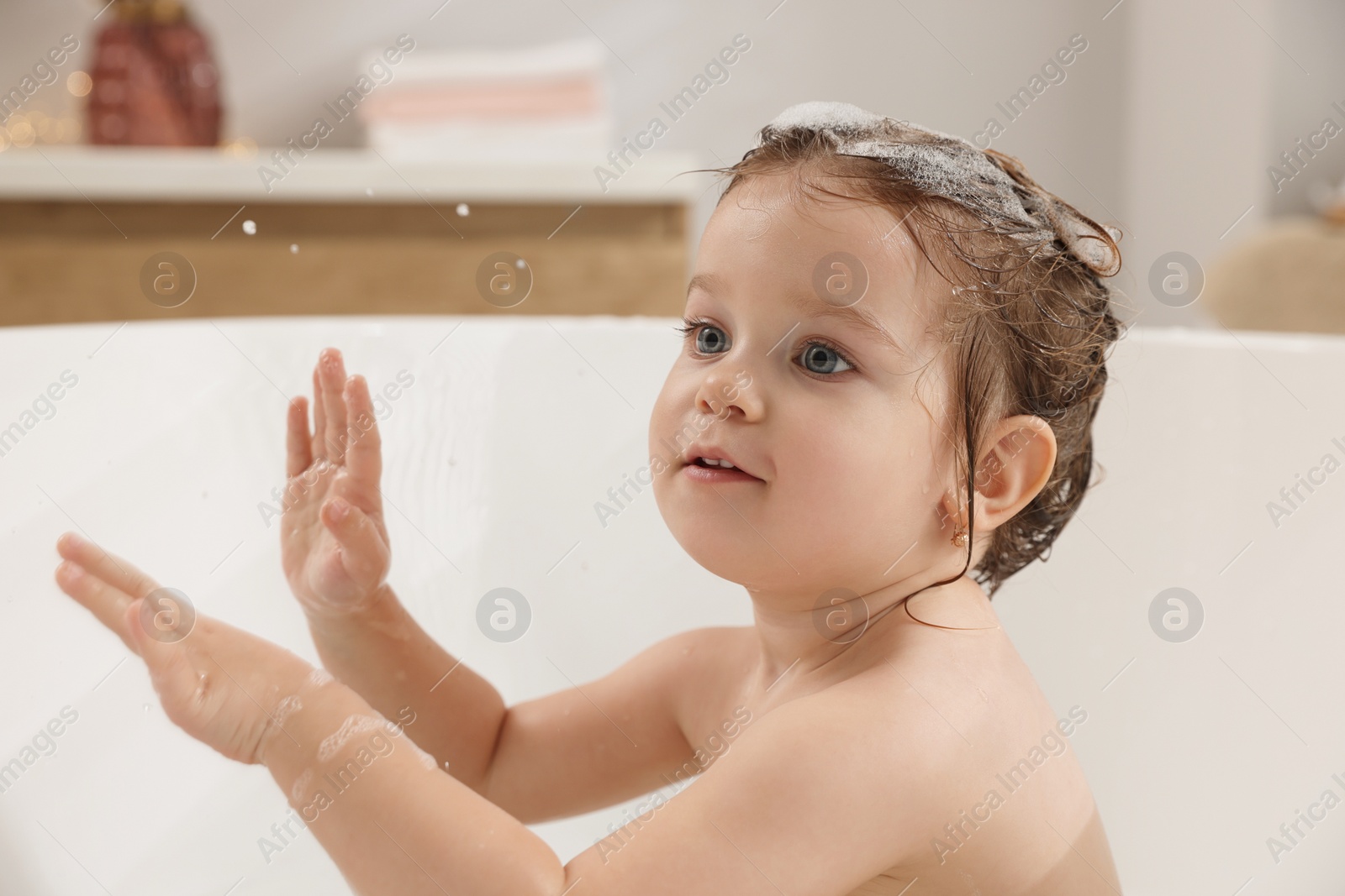 Photo of Cute little girl washing hair with shampoo in bathroom