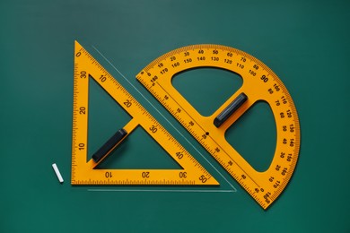 Photo of Protractor, triangle and chalk on green chalkboard, flat lay