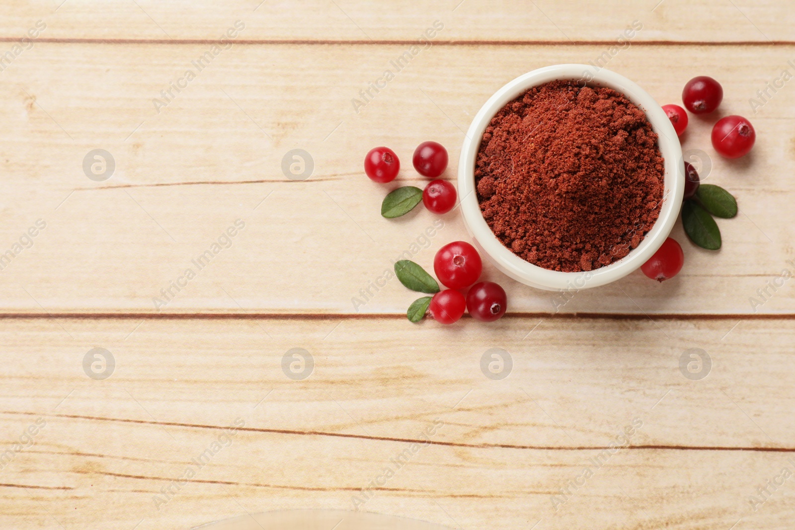 Photo of Dried cranberry powder in bowl, fresh berries and green leaves on light wooden table, top view. Space for text