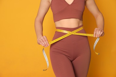 Photo of Woman in sportswear measuring waist with tape on yellow background, closeup. Space for text
