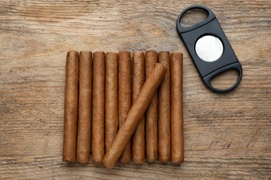 Photo of Cigars and guillotine cutter on wooden table, flat lay