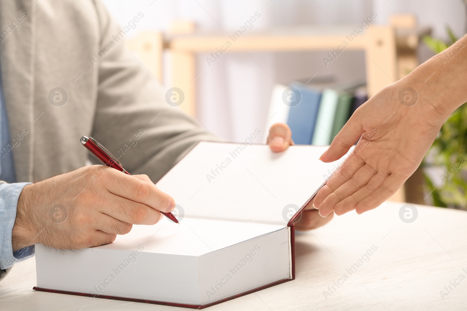 Photo of Writer signing autograph in book at table, closeup