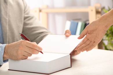 Writer signing autograph in book at table, closeup