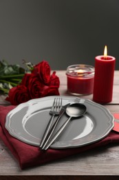 Romantic place setting with red roses and candles on wooden table. St. Valentine's day dinner