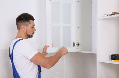 Worker installing door of cabinet in kitchen