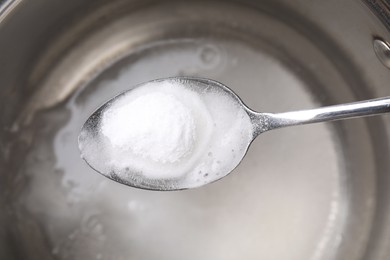 Vinegar and baking soda in spoon over saucepan, top view