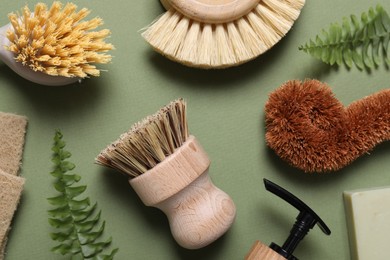 Photo of Cleaning brushes, sponges, dispenser and fern leaves on green background, flat lay