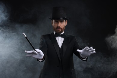 Photo of Magician holding wand in smoke on black background