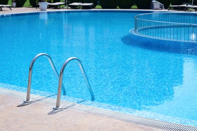 Outdoor swimming pool with ladder and handrails on sunny day, space for text