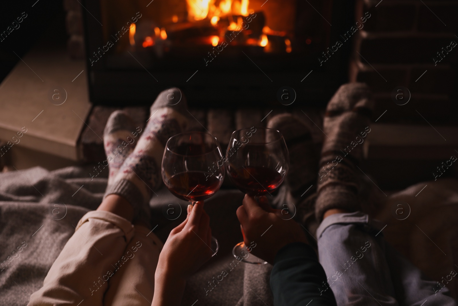 Photo of Couple with glasses of red wine near burning fireplace, closeup