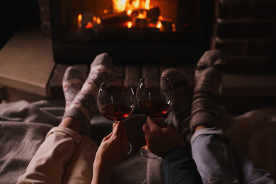 Couple with glasses of red wine near burning fireplace, closeup