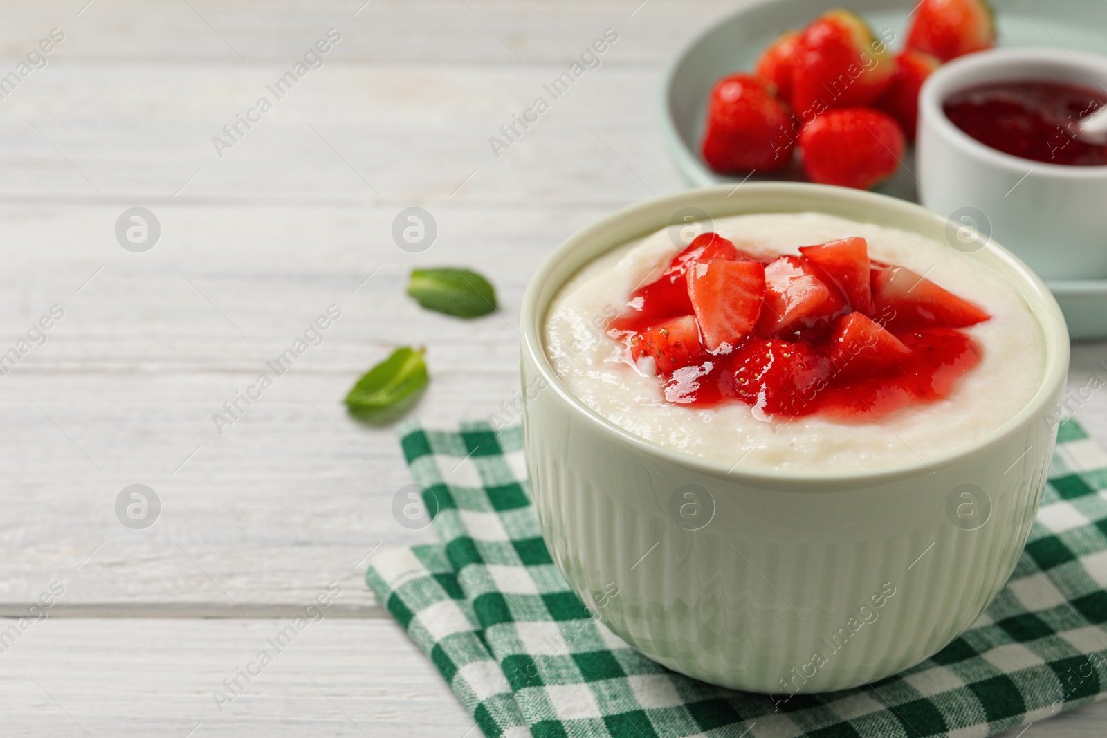 Photo of Delicious semolina pudding with strawberries and jam on white wooden table, space for text