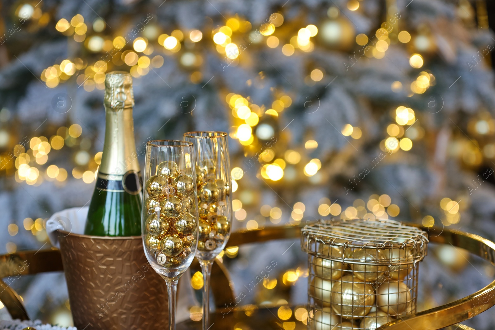 Photo of Glasses, baubles, bottle of sparkling wine and other Christmas decor on table against blurred background, closeup