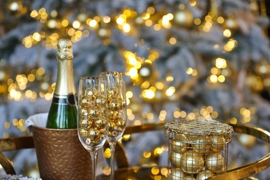 Photo of Glasses, baubles, bottle of sparkling wine and other Christmas decor on table against blurred background, closeup