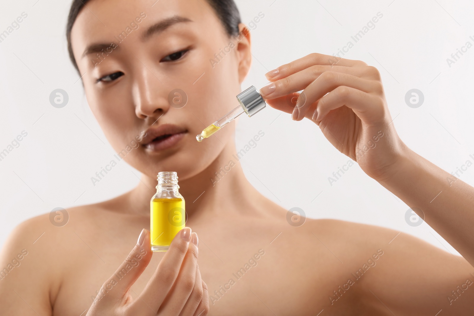 Photo of Beautiful young woman with bottle of cosmetic serum on white background, selective focus