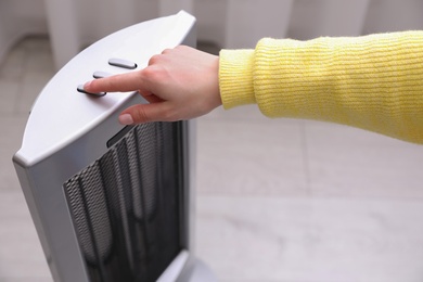 Photo of Woman turning on modern heater indoors, closeup