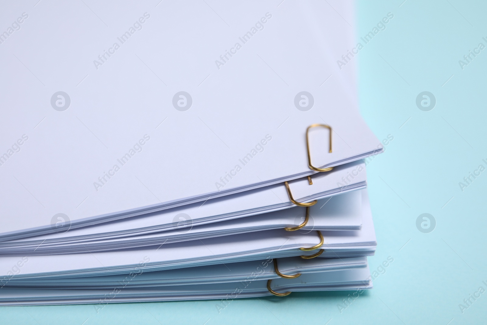 Photo of Sheets of paper with clips on light blue background, closeup