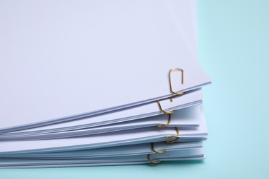 Photo of Sheets of paper with clips on light blue background, closeup