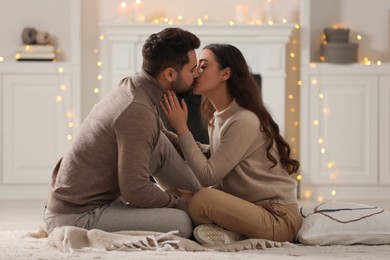 Photo of Cute young couple kissing on soft carpet at home