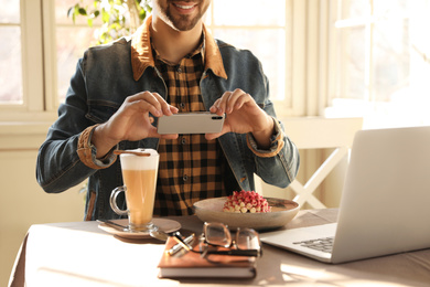 Young blogger taking picture of dessert at table in cafe, closeup