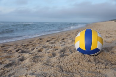 Colorful volleyball ball on sand near sea. Space for text