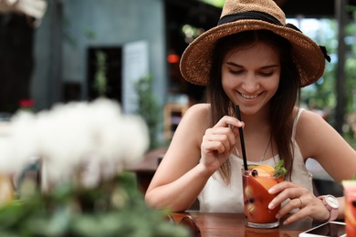 Woman with glass of tasty lemonade at table in cafe