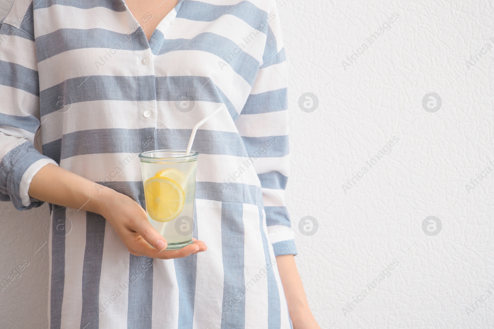 Photo of Young woman holding glass with lemon cocktail against light background