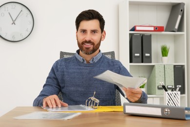 Photo of Businessman holding document at wooden table in office