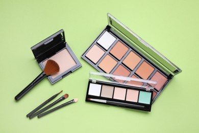Photo of Colorful contouring palettes with brushes on light green background, flat lay. Professional cosmetic product