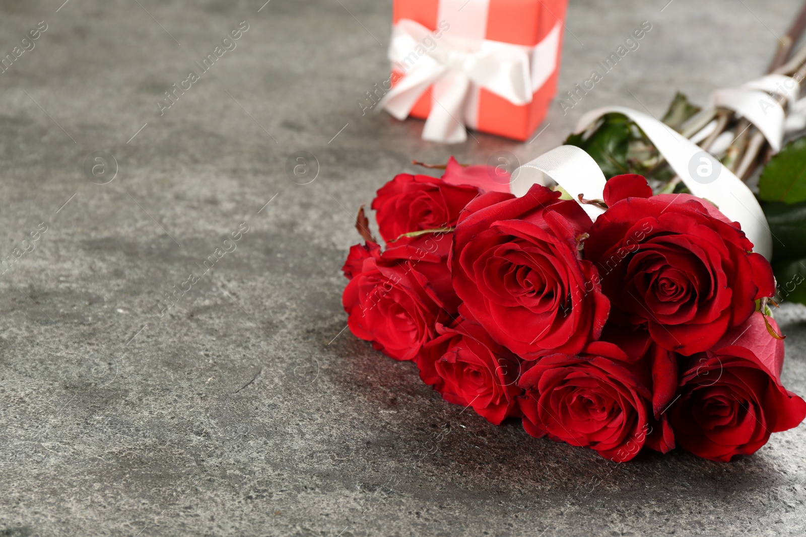 Photo of Beautiful red roses and gift box on grey table, space for text. Valentine's Day celebration