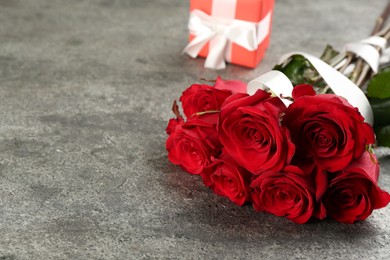 Beautiful red roses and gift box on grey table, space for text. Valentine's Day celebration