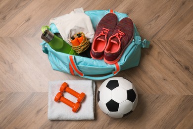 Photo of Blue gym bag and sports accessories on wooden floor, flat lay