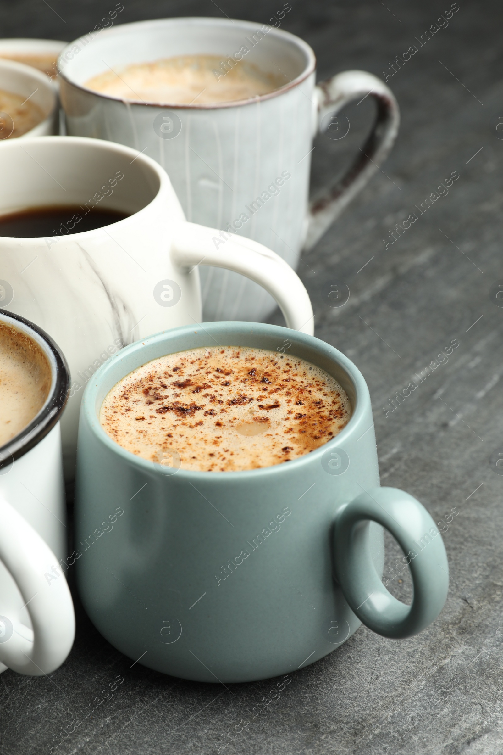 Photo of Many cups of different coffees on slate table, closeup