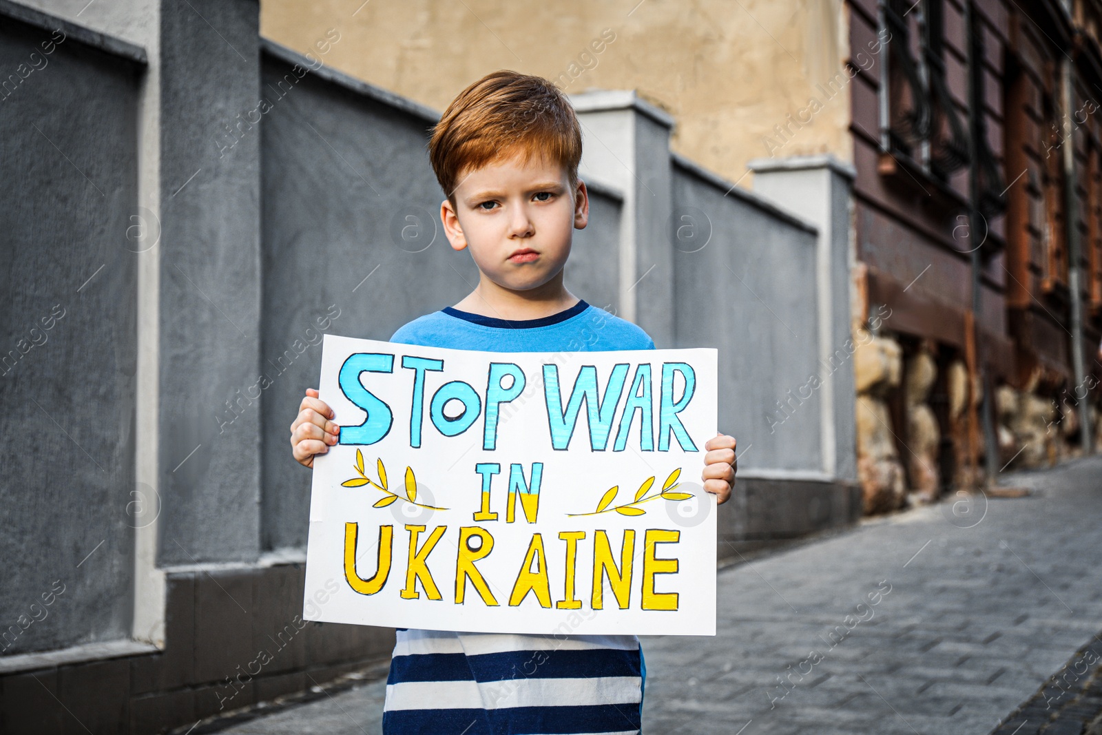 Photo of Sad boy holding poster in colors of national flag with words Stop War In Ukraine on city street