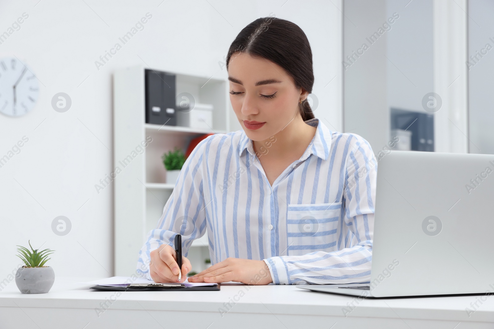 Photo of Young female intern working with laptop at table in office