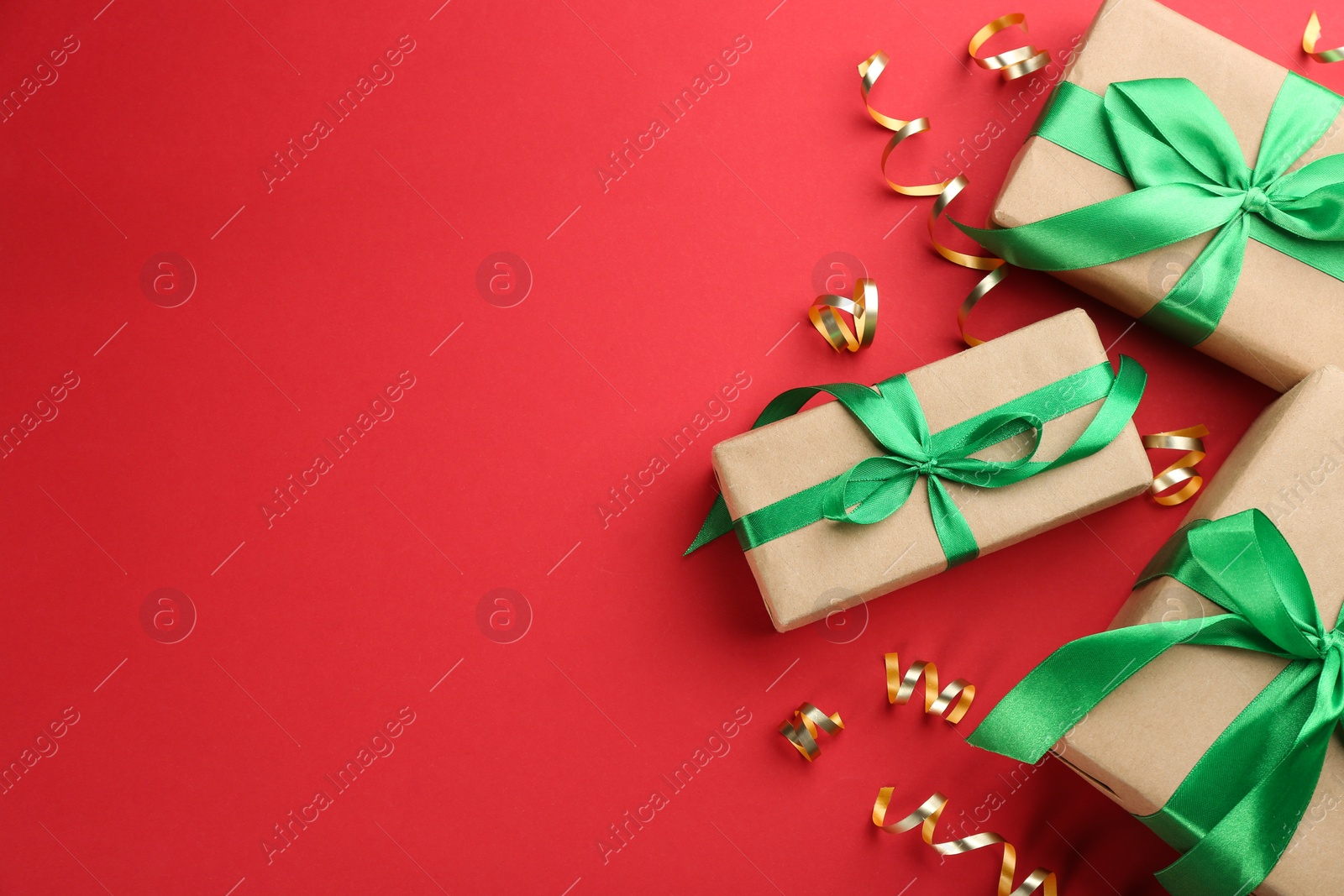 Photo of Shiny serpentine streamers and Christmas gifts on red background, flat lay. Space for text