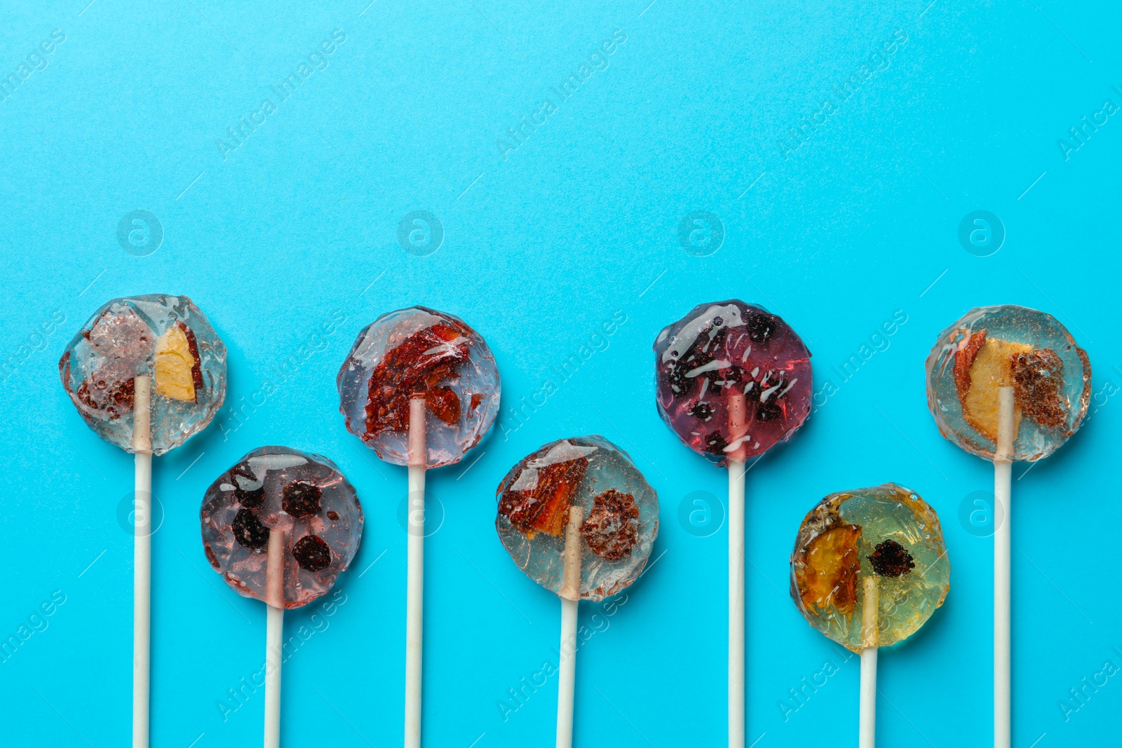 Photo of Sweet colorful lollipops with berries on light blue background, flat lay