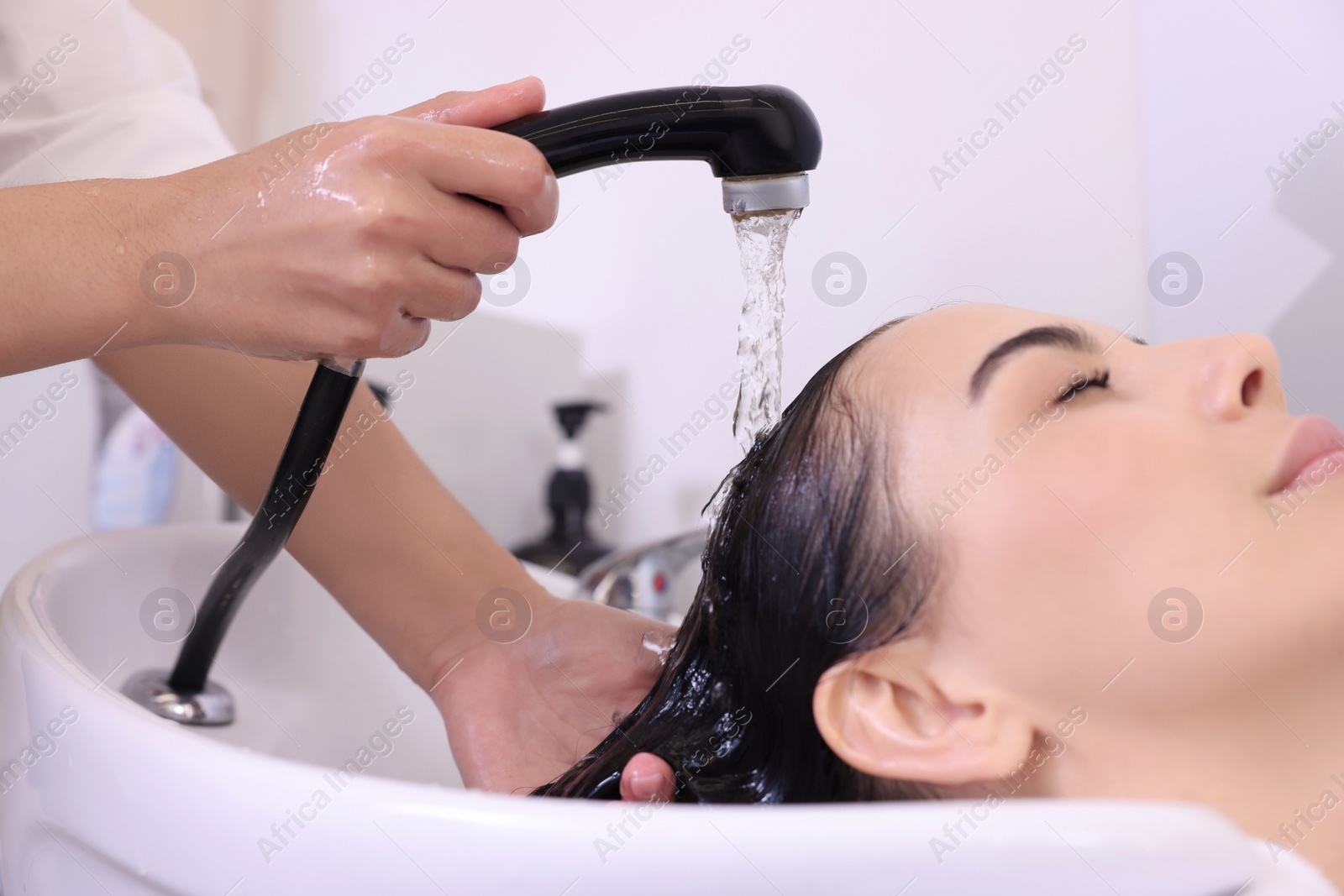 Photo of Professional hairdresser washing woman's hair in beauty salon, closeup