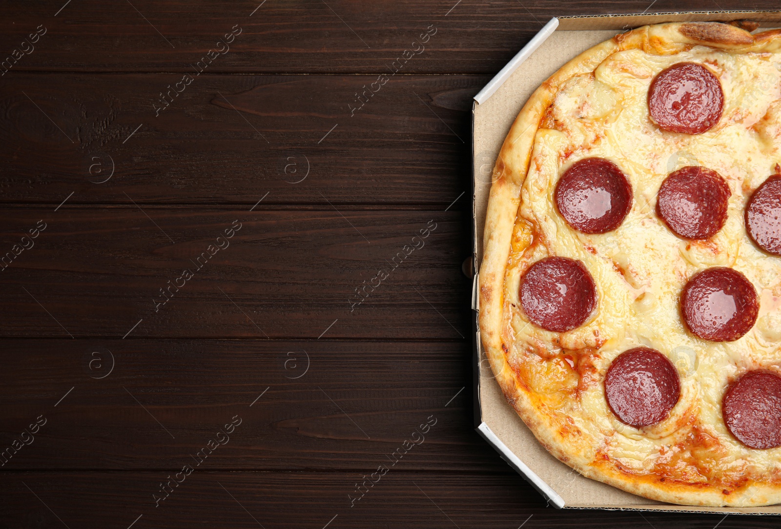 Photo of Tasty pepperoni pizza in cardboard box on wooden table, top view. Space for text