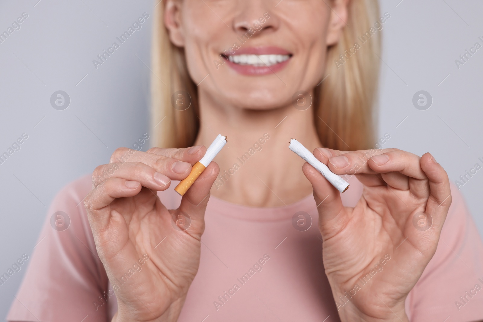 Photo of Woman with broken cigarette on light grey background, closeup. Stop smoking concept